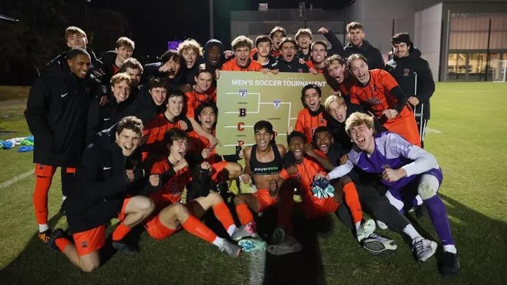 A mens soccer team team celebrates and poses for picture in front of printout tournament bracket.