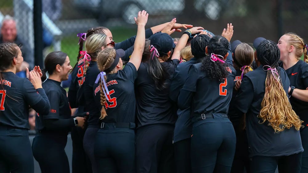Group of softball players in navy blue and orange uniforms celebrate together around home plate. 