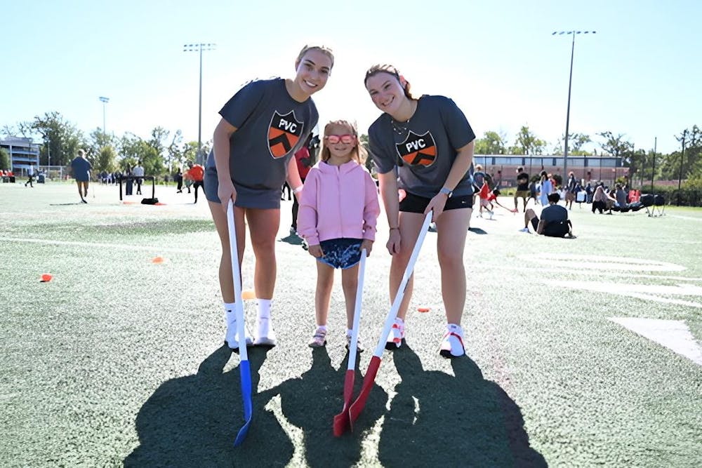 Two field hockey athletes stand on either side of a youth athlete.