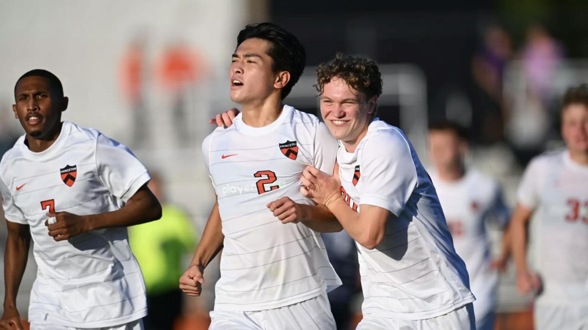 Three players in white and orange jerseys celebrate together
