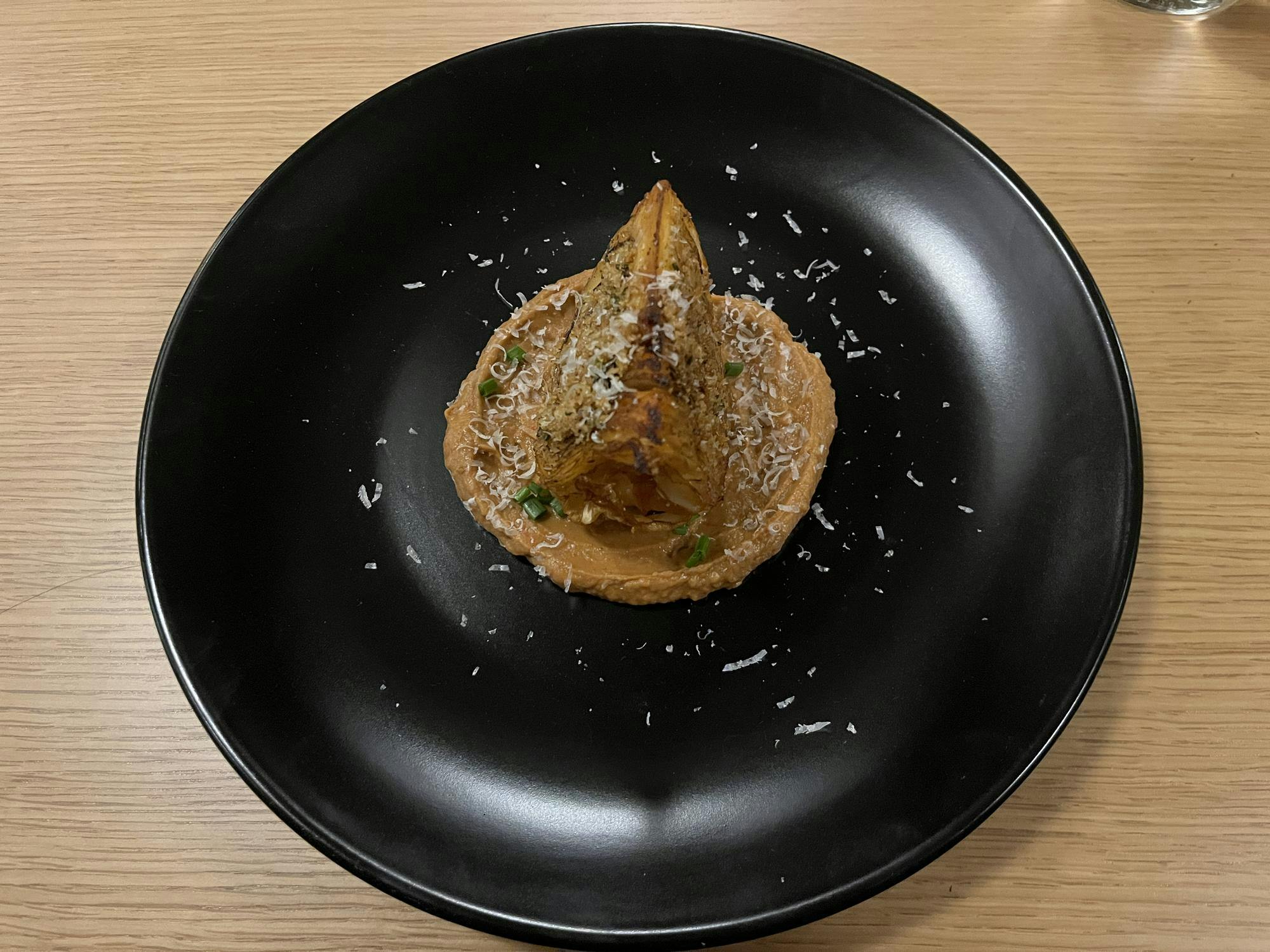 A black plate has a brown cabbage covered in brown sauce sprinkled with white cheese flakes.