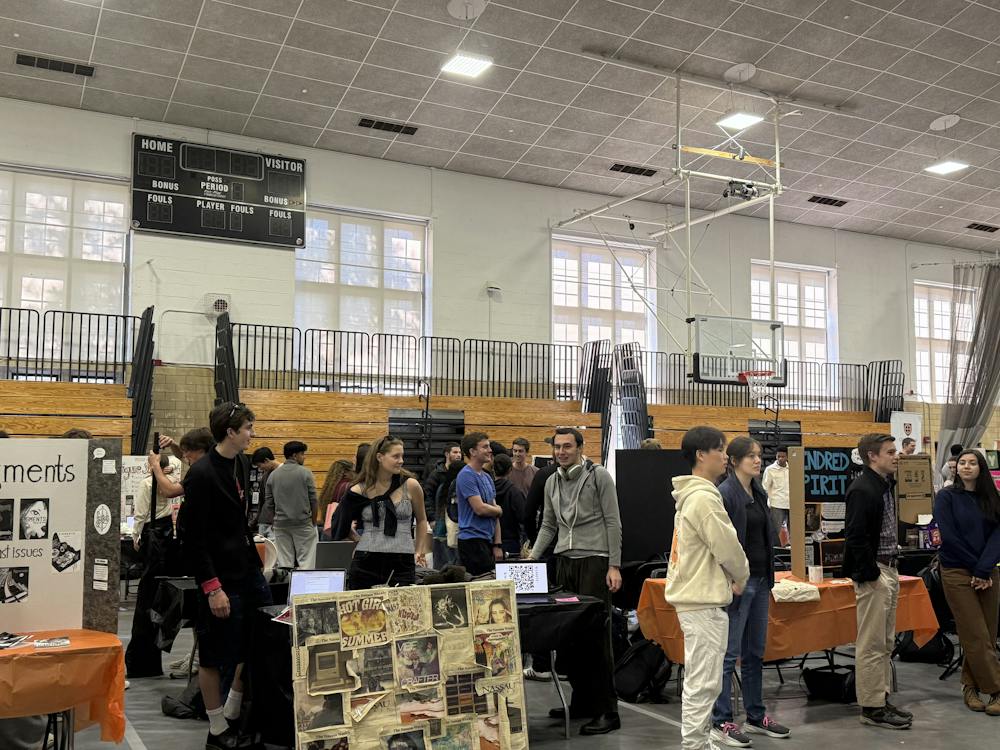 Students gather around tables in an indoor gym. 