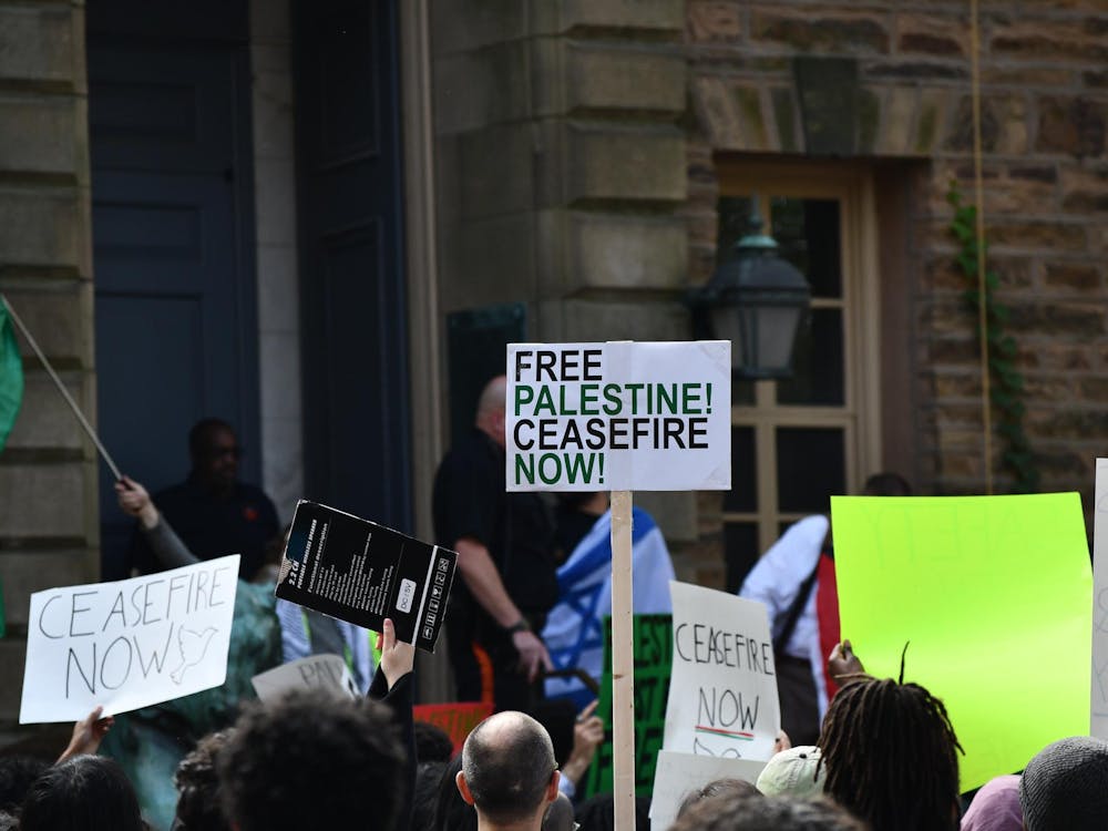 A number of people hold up signs reading "Free Palestine Ceasefire Now" and "Ceasefire Now" holding Palestinian flags. A person holding an Israeli flag is visible in the background.