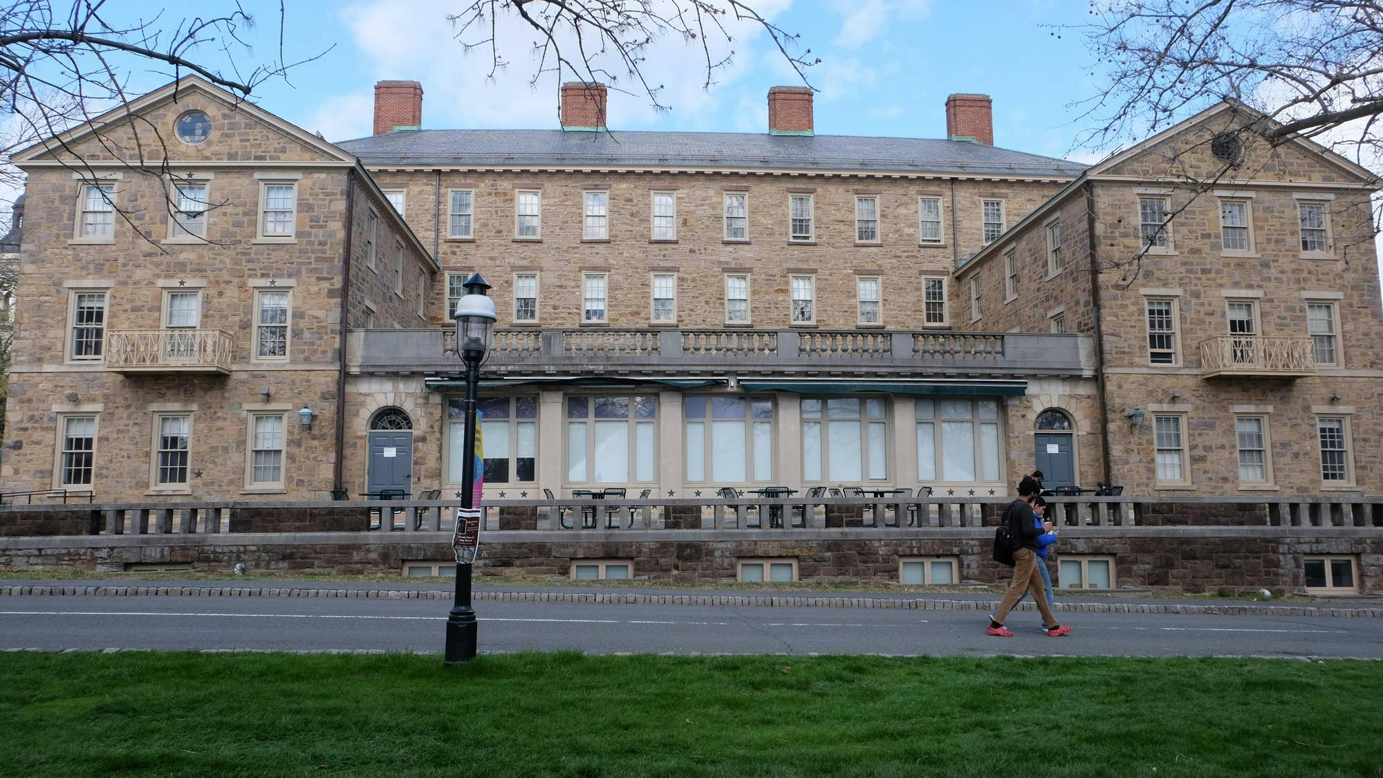 The back of a stone building featuring large windows and a balcony, surrounded by grass. 