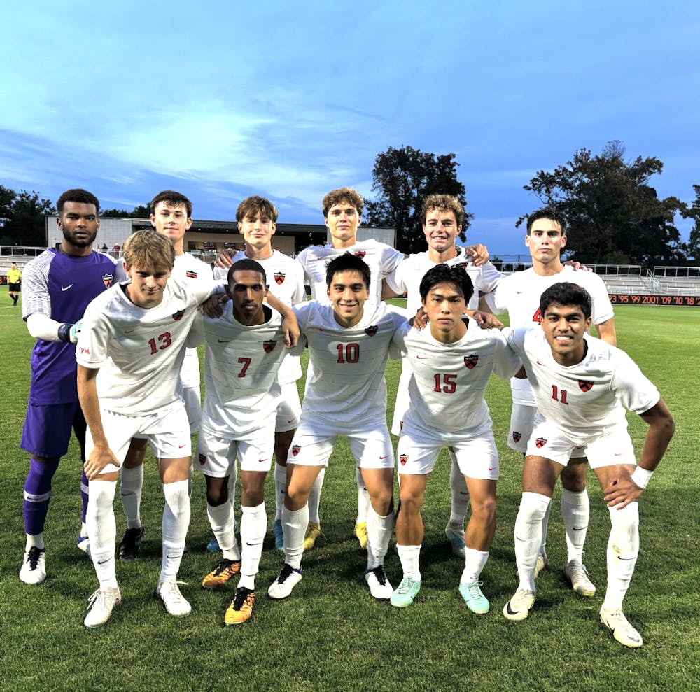 Image of eleven soccer players in white uniforms huddled together pre-game. 