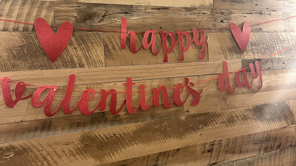 Red letters spelling out “Happy Valentine’s Day” sits against a wood-paneled wall.