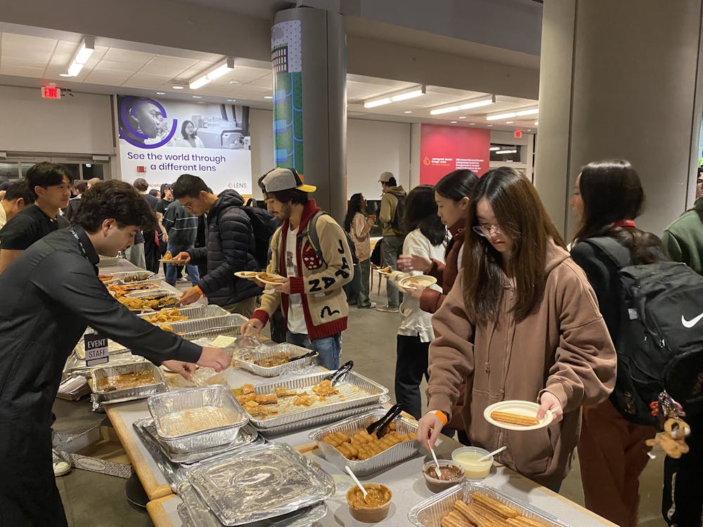 Over 30 students are in the photo taking food from various containers and socializing. 