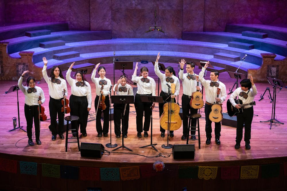 Ten members of of the Mariachi band take a bow after their first performance, instruments in hand and smiling. 