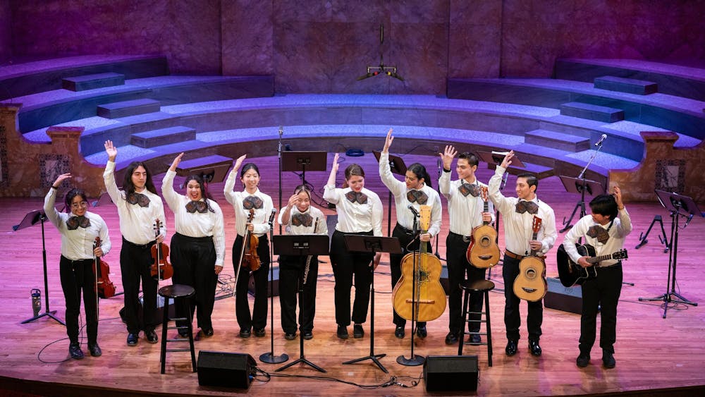 Ten members of of the Mariachi band take a bow after their first performance, instruments in hand and smiling. 