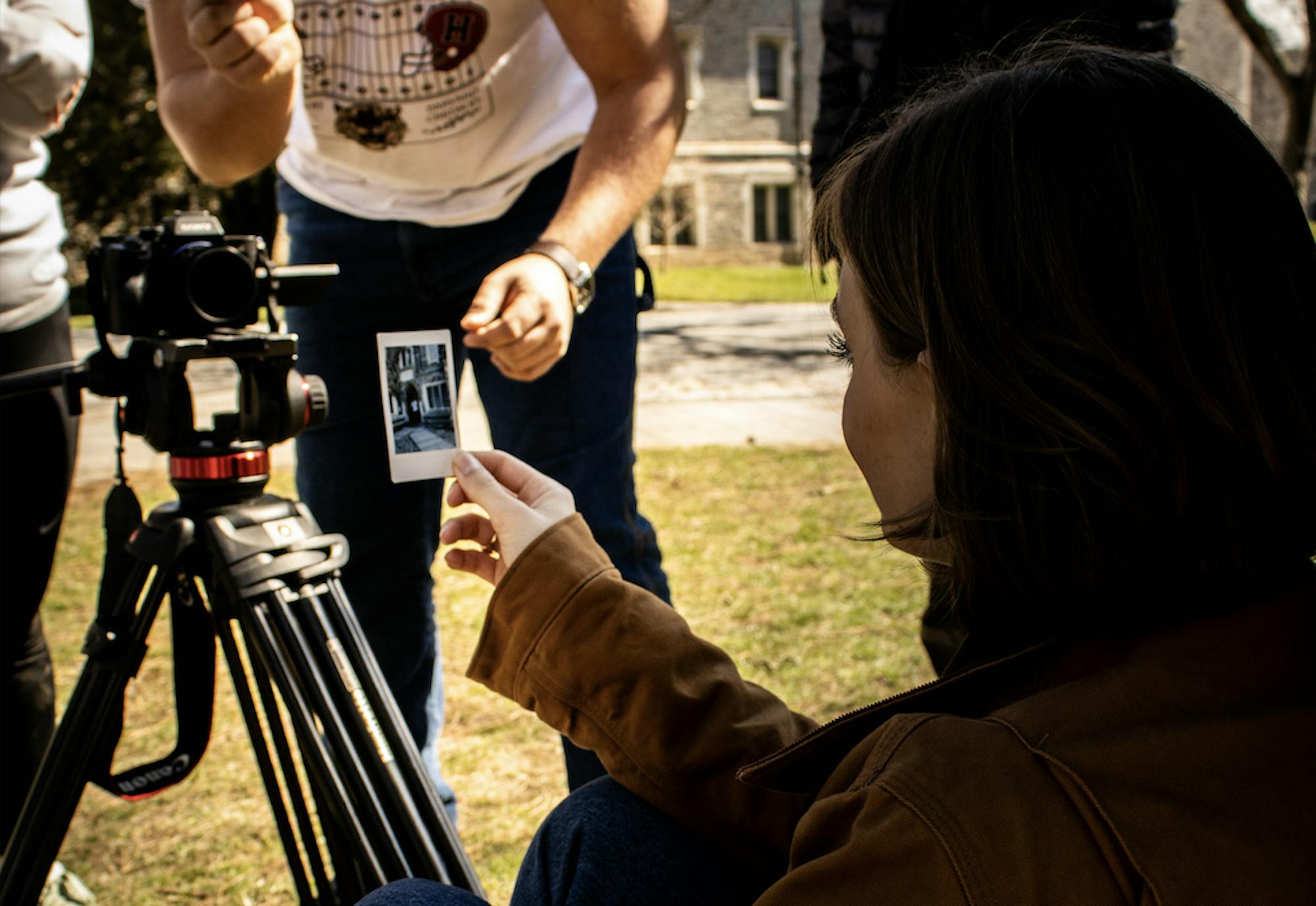 A person wearing a brown jacket with short blond hair is holding up a small photo with a white border.