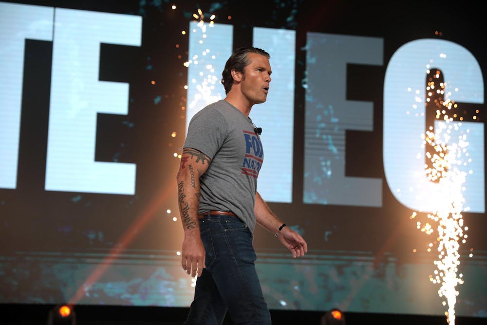 Muscular white man with arm tattoos wearing jeans and a tight-fitting gray t-shirt on a stage.