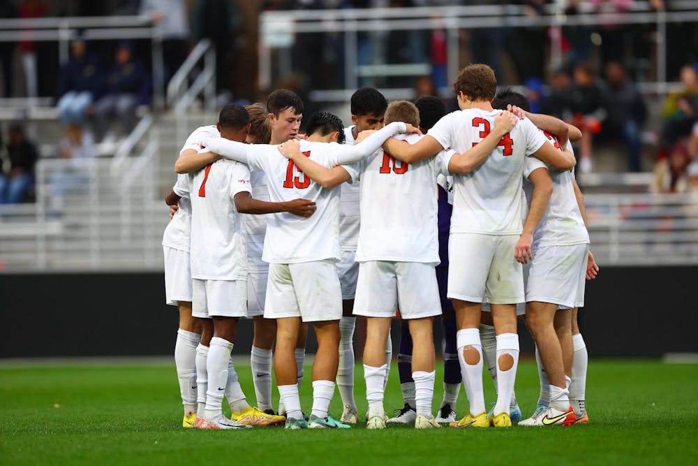 Male soccer players in white jerseys huddle up on soccer field.