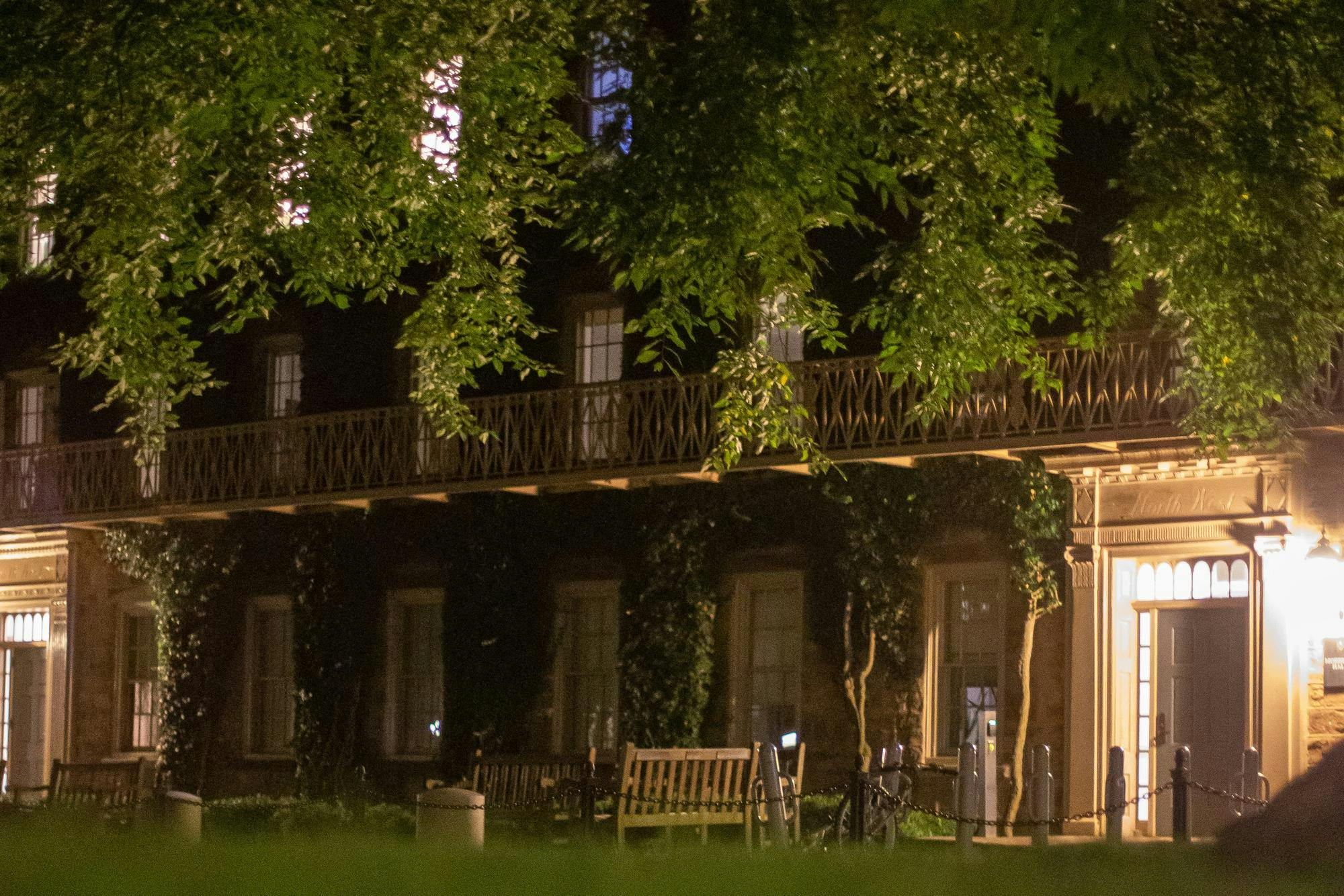 A stone building is illuminated with warm light. There's a bench outside.