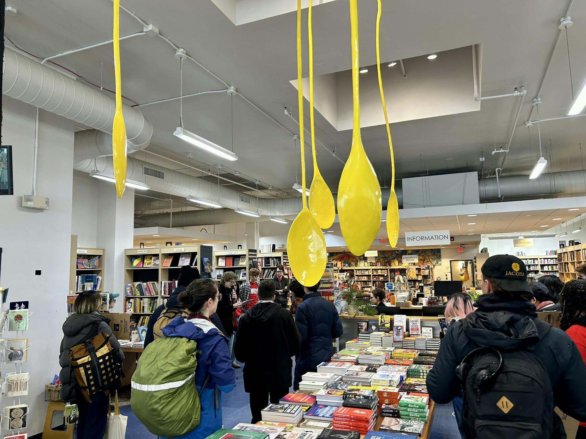 About fifteen people are shown gathered around a table of books, with one person holding a microphone.