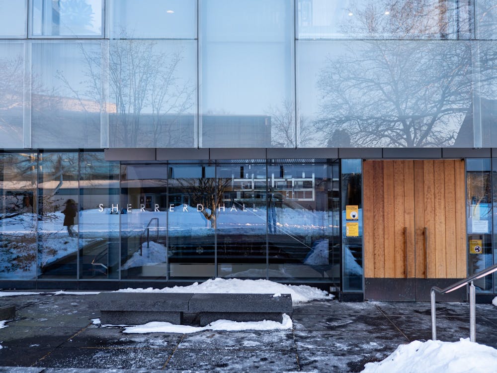 Glass building with wood doors. In the foreground, a sidewalk with snow.
