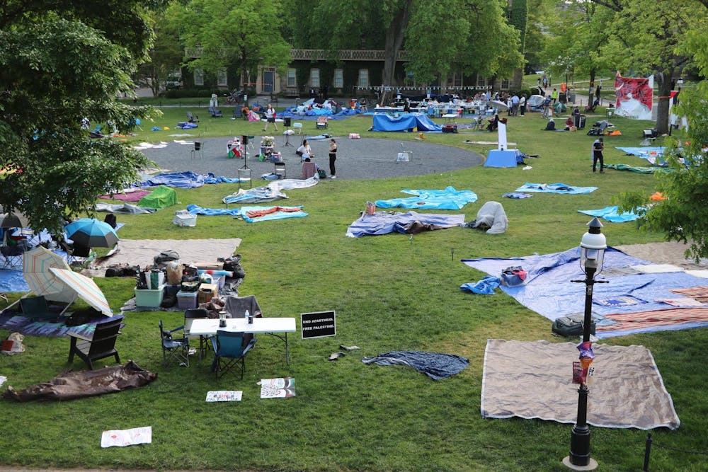 A green field with scattered tarps, umbrellas, and signs