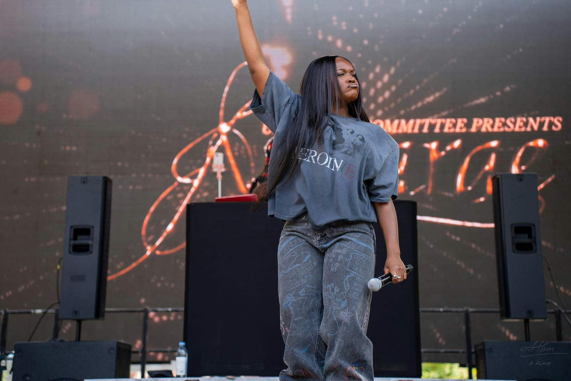 A woman is standing on a stage with one arm raised in the air and the other hand holding a microphone.
