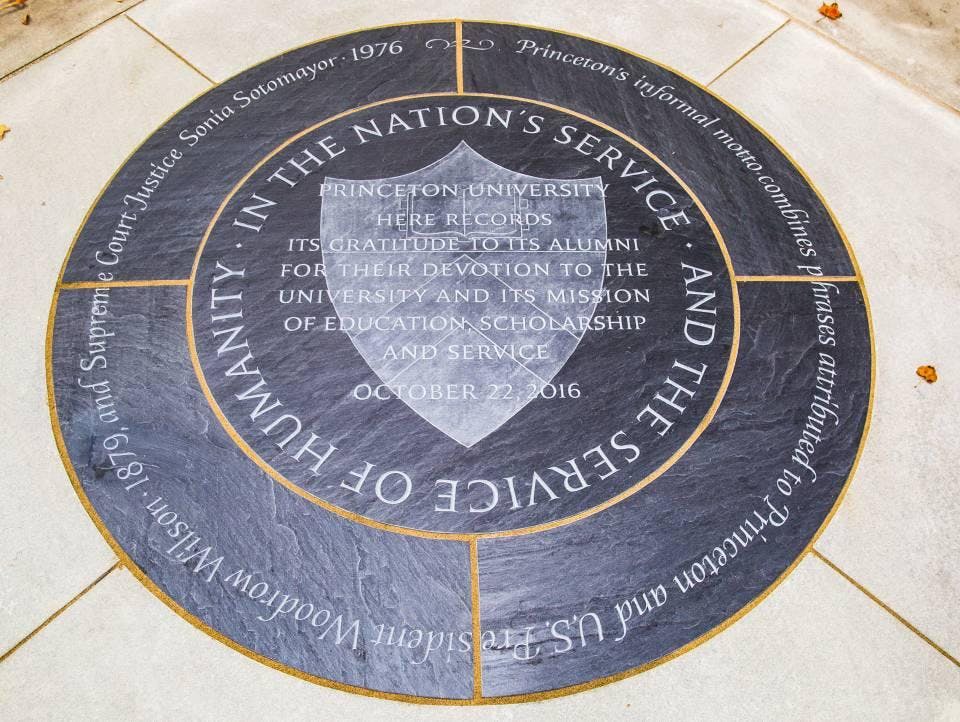 Photo of a black and gold seal on the stone floor of Nassau Hall displaying Princeton’s unofficial motto: “In the nation’s service and the service of humanity.”
