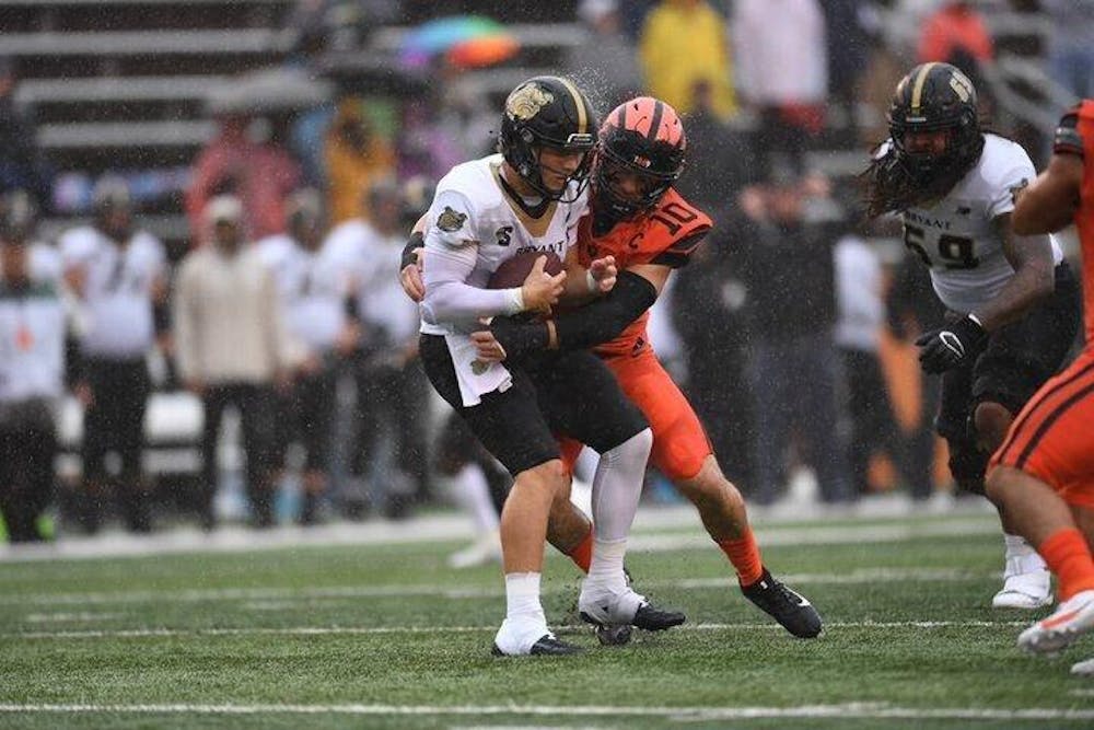 As rain pours, a man in a orange jersey tackles a man in a white jersey holding a football. 