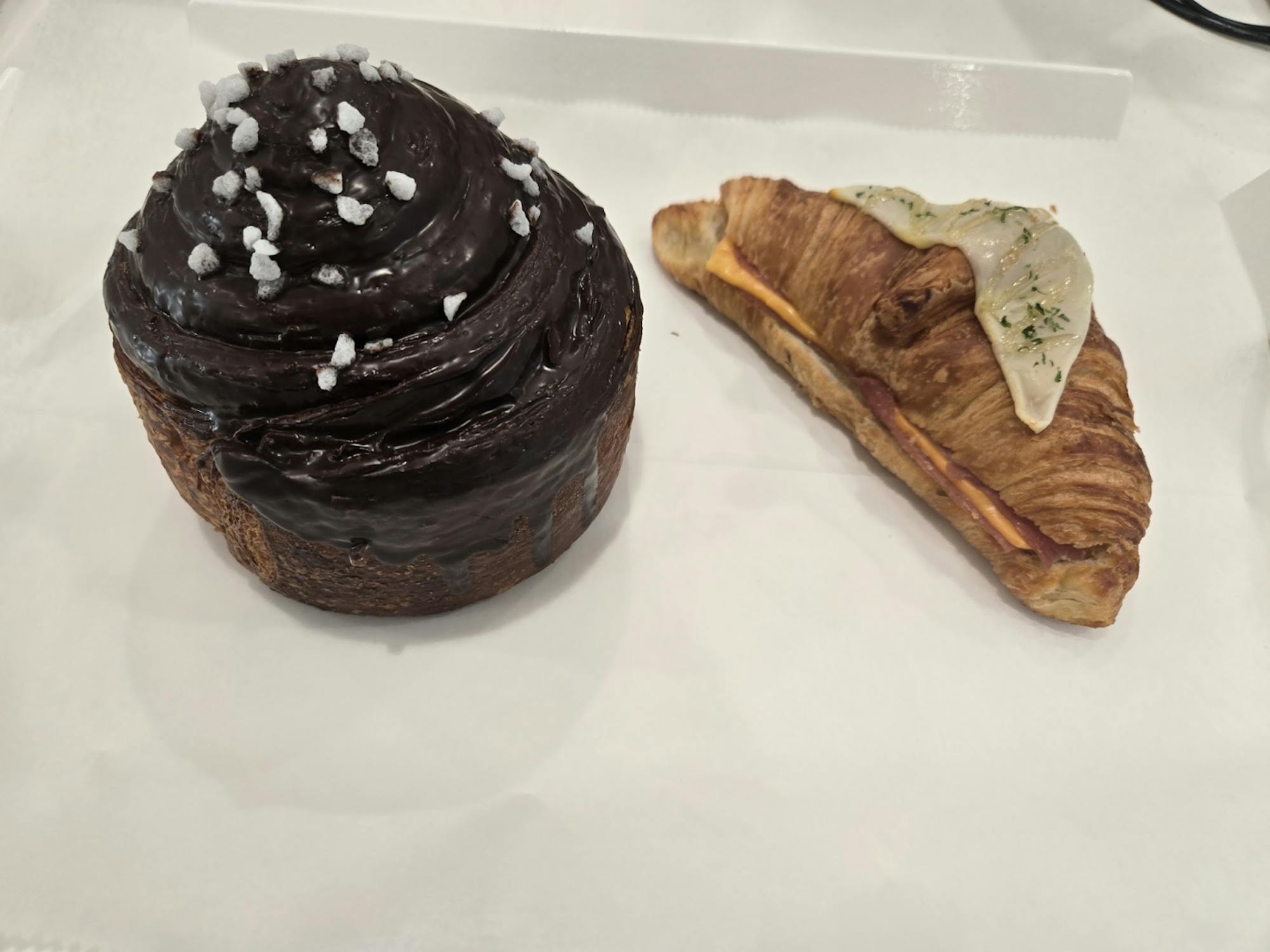 A chocolate croissant pastry and a croissant with sliced ham and cheese on a parchment paper.