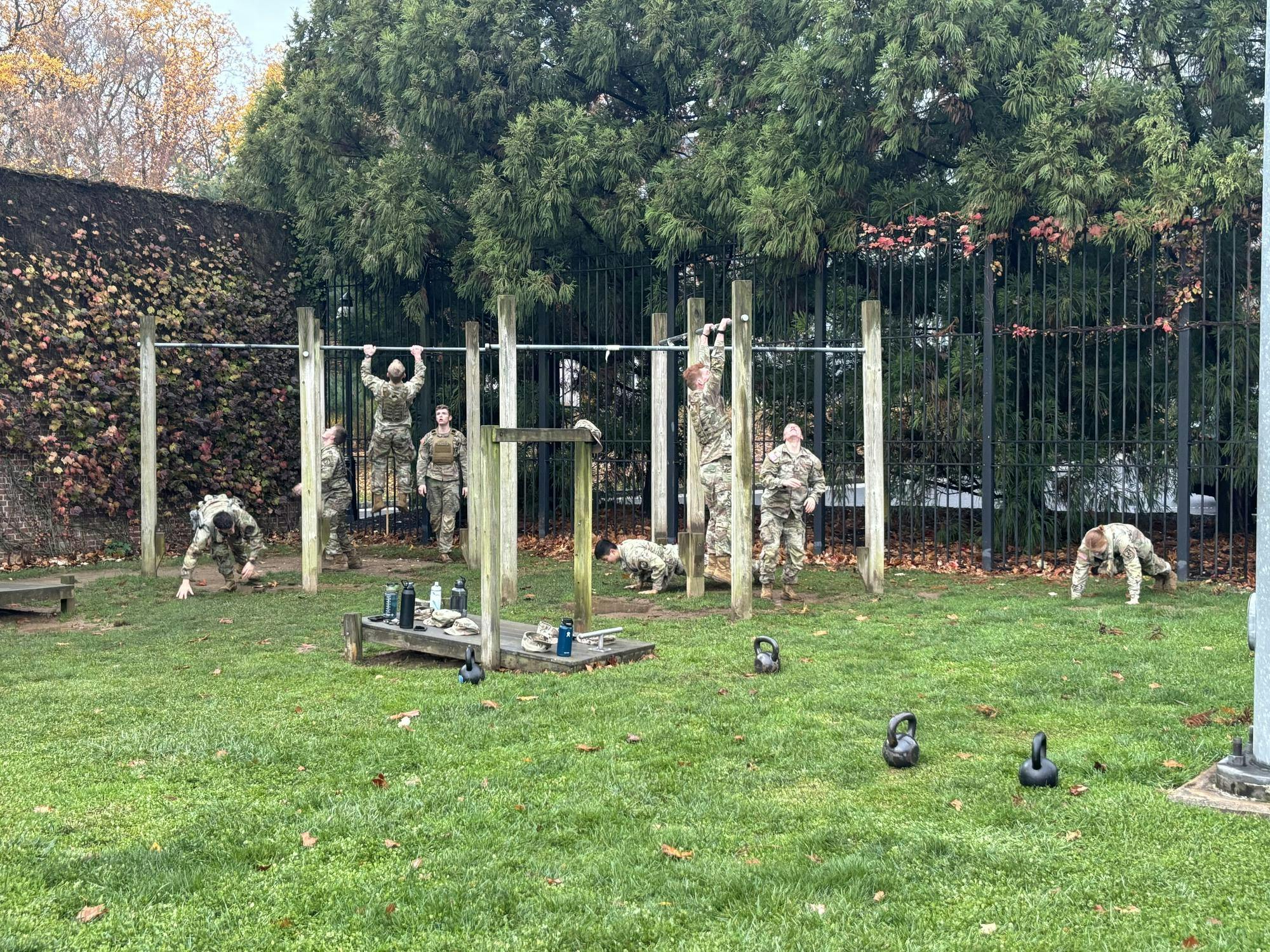 A group of ROTC cadets in a grass field completing pushups into pullups on lateral bars.