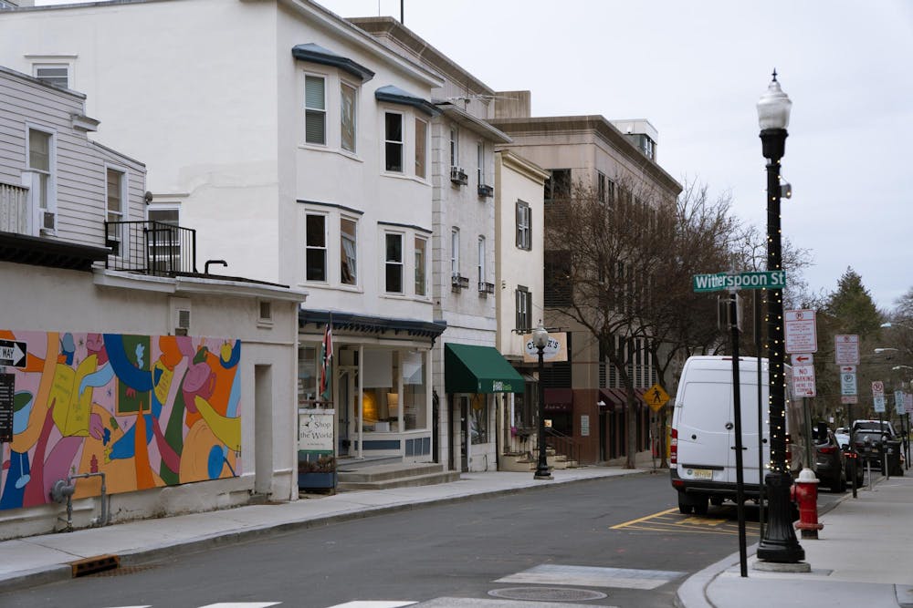 A green street sign reading “Witherspoon St,” with a row of storefronts and a colorful mural in the background.