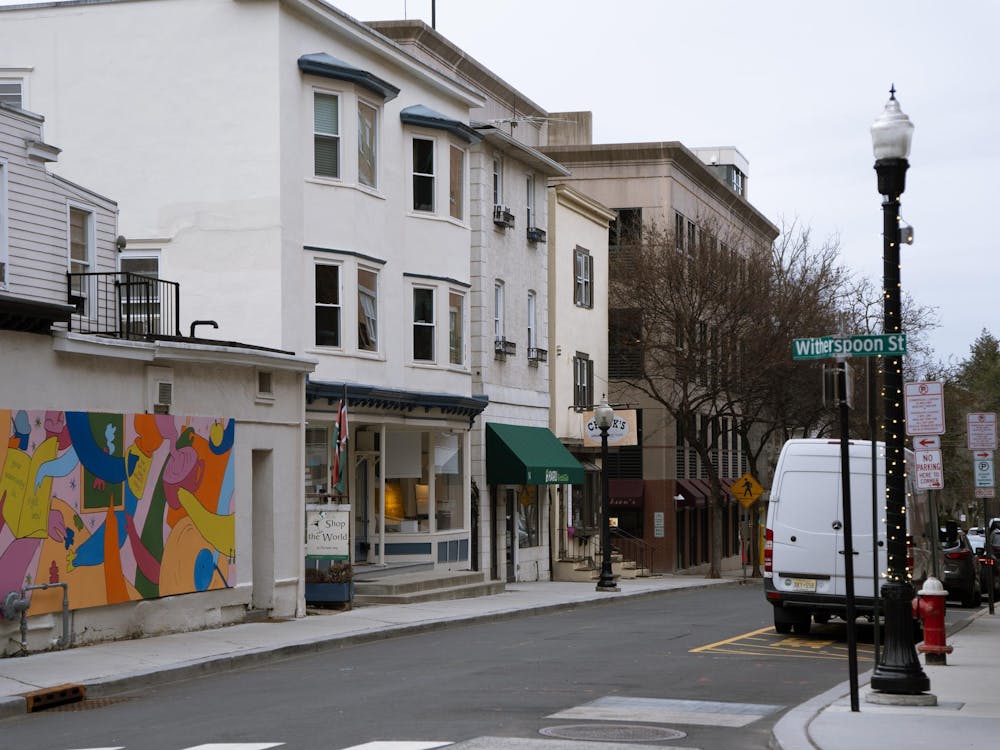 A green street sign reading “Witherspoon St,” with a row of storefronts and a colorful mural in the background.