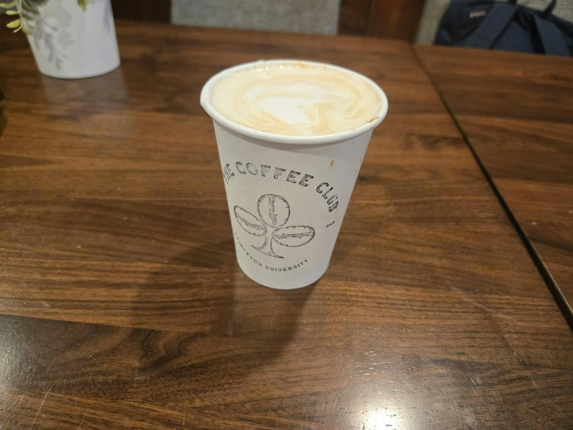 Paper cup with stamped ‘Coffee Club’ logo, filled with foamy drink.