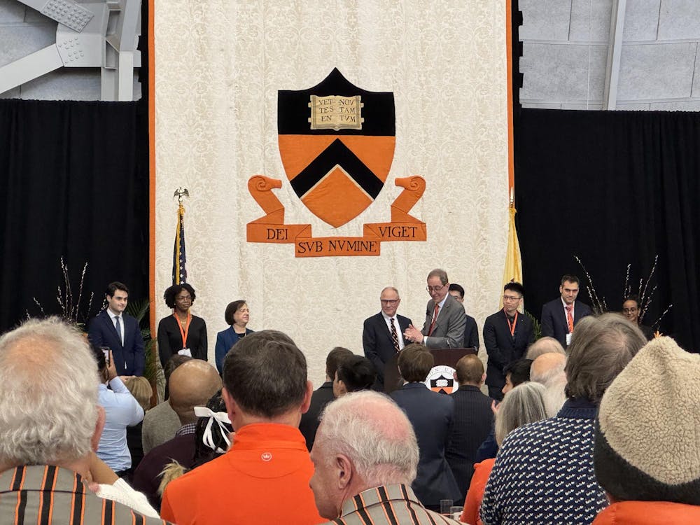 A large white panel with Princeton's shield and Latin motto in the background. A number of people stand in front of it.