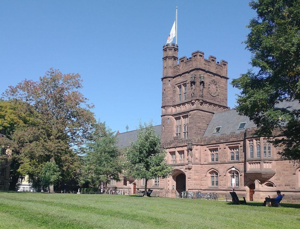 A green lawn and courtyard in front of a gothic style building on a sunny day.