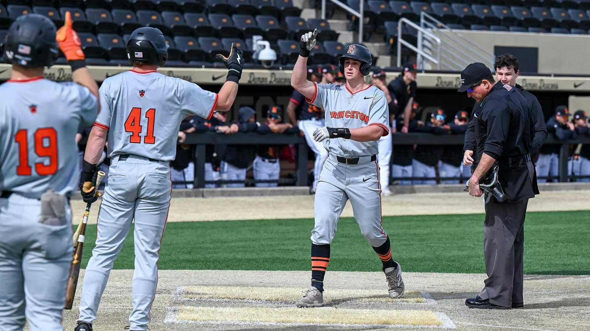 Baseball player in grey uniform runs to homeplate where two teammates are waiting.