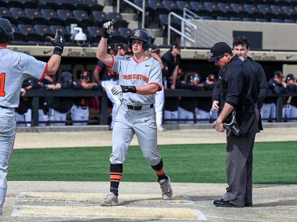 Baseball player in grey uniform runs to homeplate where two teammates are waiting.