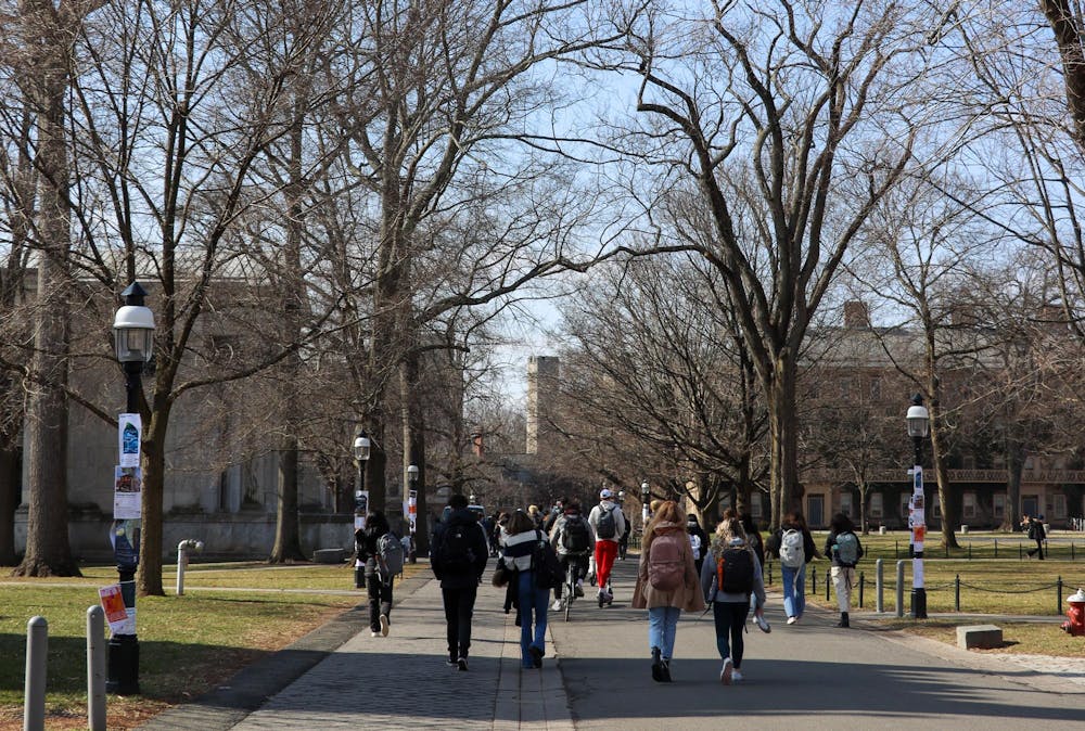 Students walk on campus with coats. Trees in the background barren.