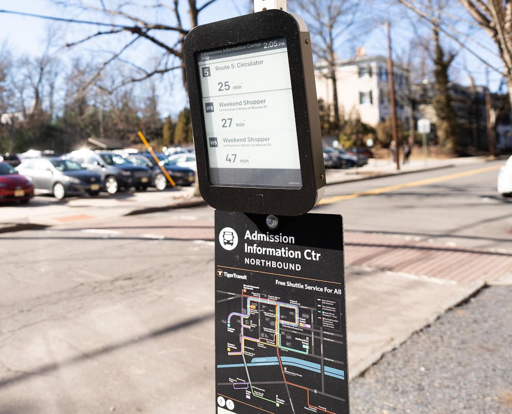 Board with bus times displays three bus routes and the times for them to arrive in black on a white background. The board sits above a route map.