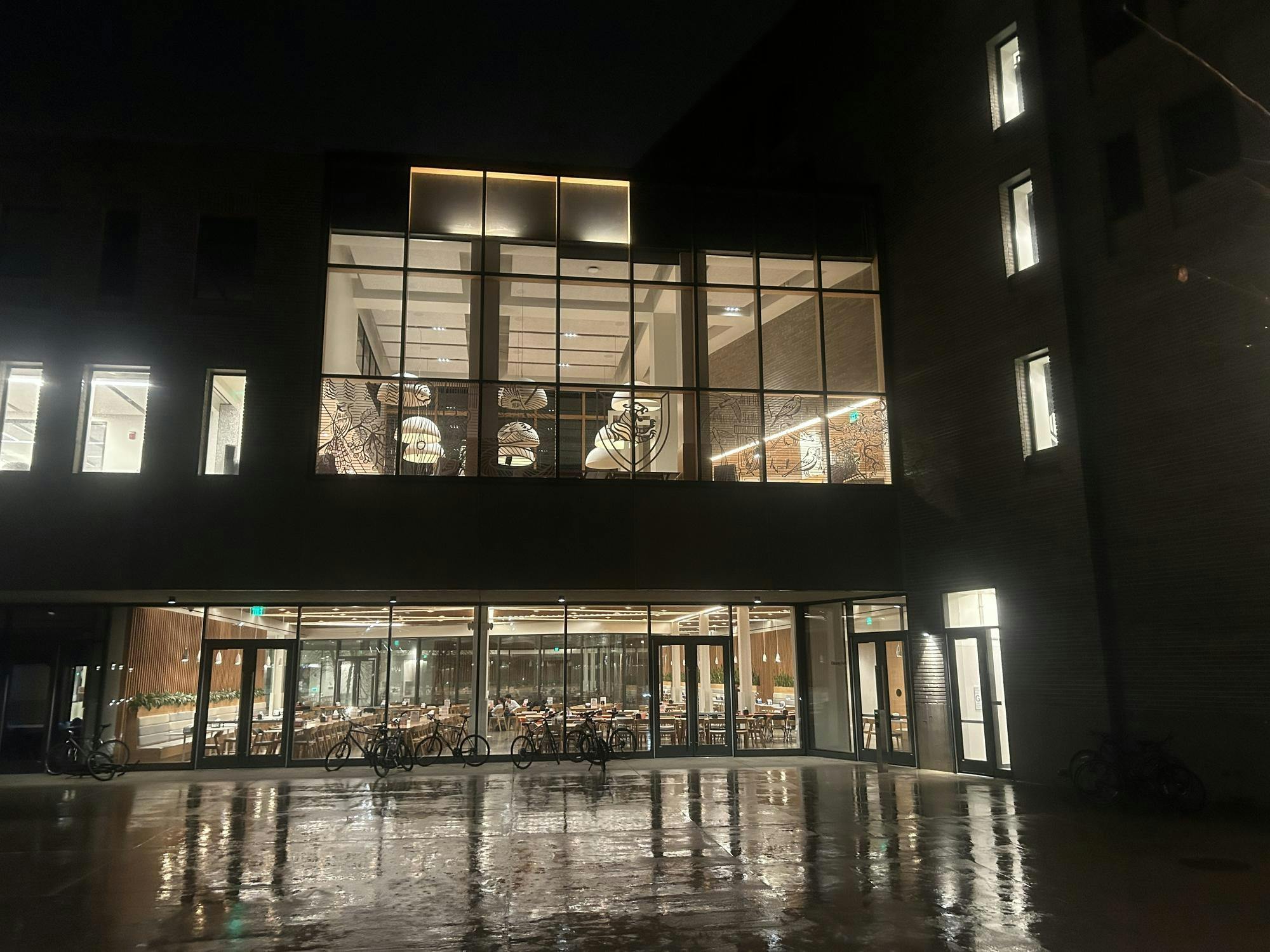 A modern, well-lit building on a rainy night in the dark, with one floor of the building's windows covered with bird-safe adornments.