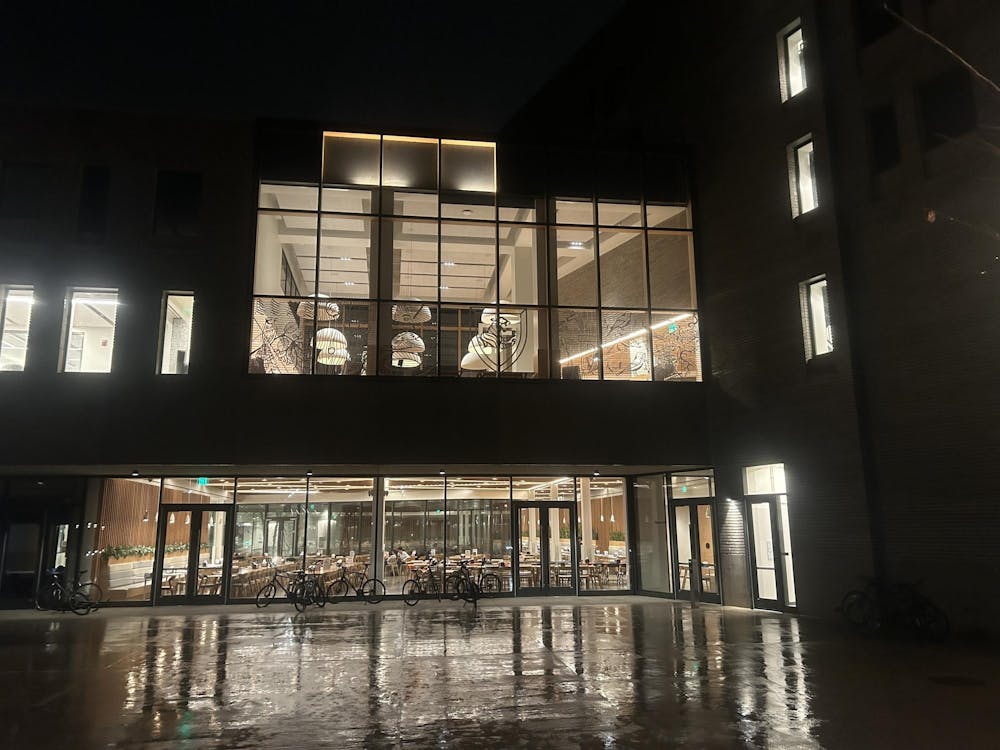A modern, well-lit building on a rainy night in the dark, with one floor of the building's windows covered with bird-safe adornments.