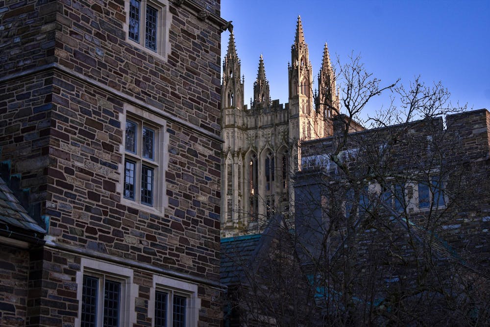 Gothic, stone building in the shade with illuminated gothic tower in the background.