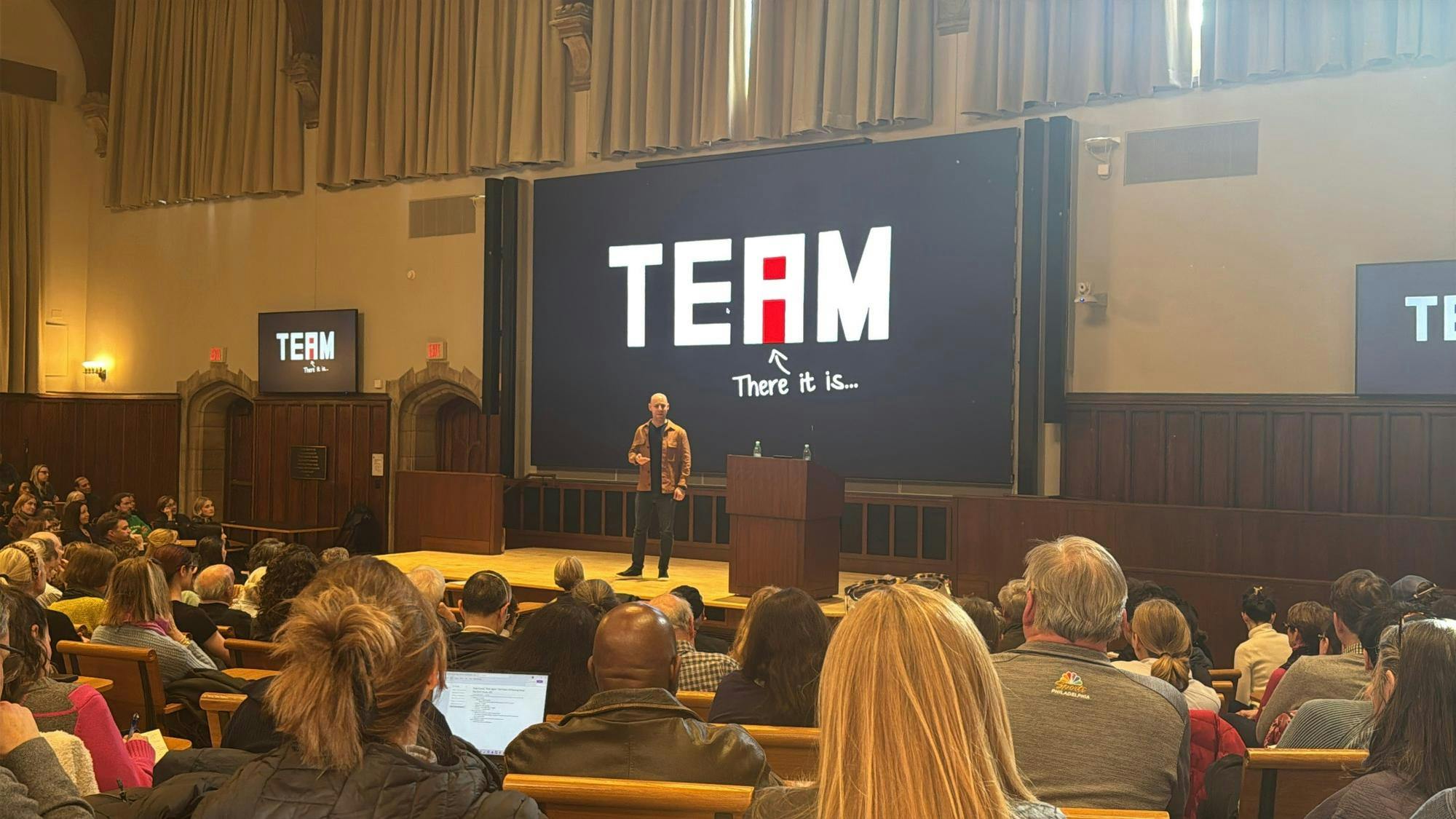 A man on a stage giving a lecture in front of a packed audience.