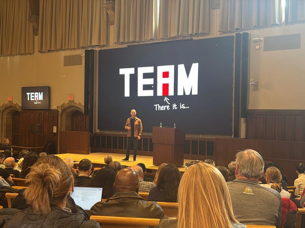 A man on a stage giving a lecture in front of a packed audience.