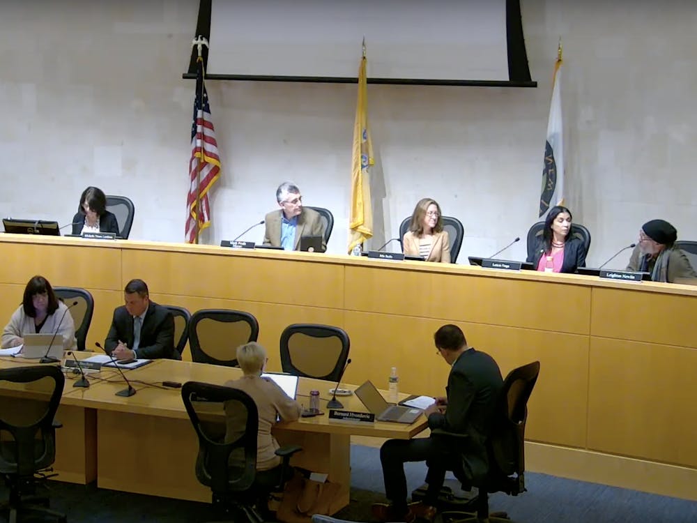 Four councilmembers look onto a fifth member who is speaking at a town council meeting.