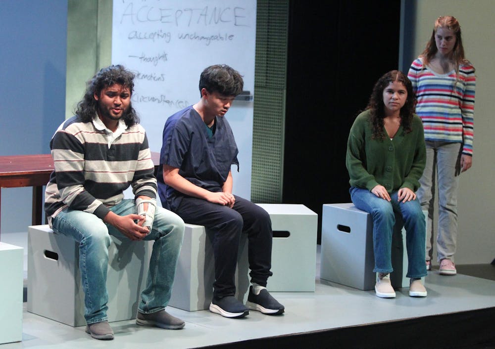 Student performers sit on cubes on stage, mid-performance.