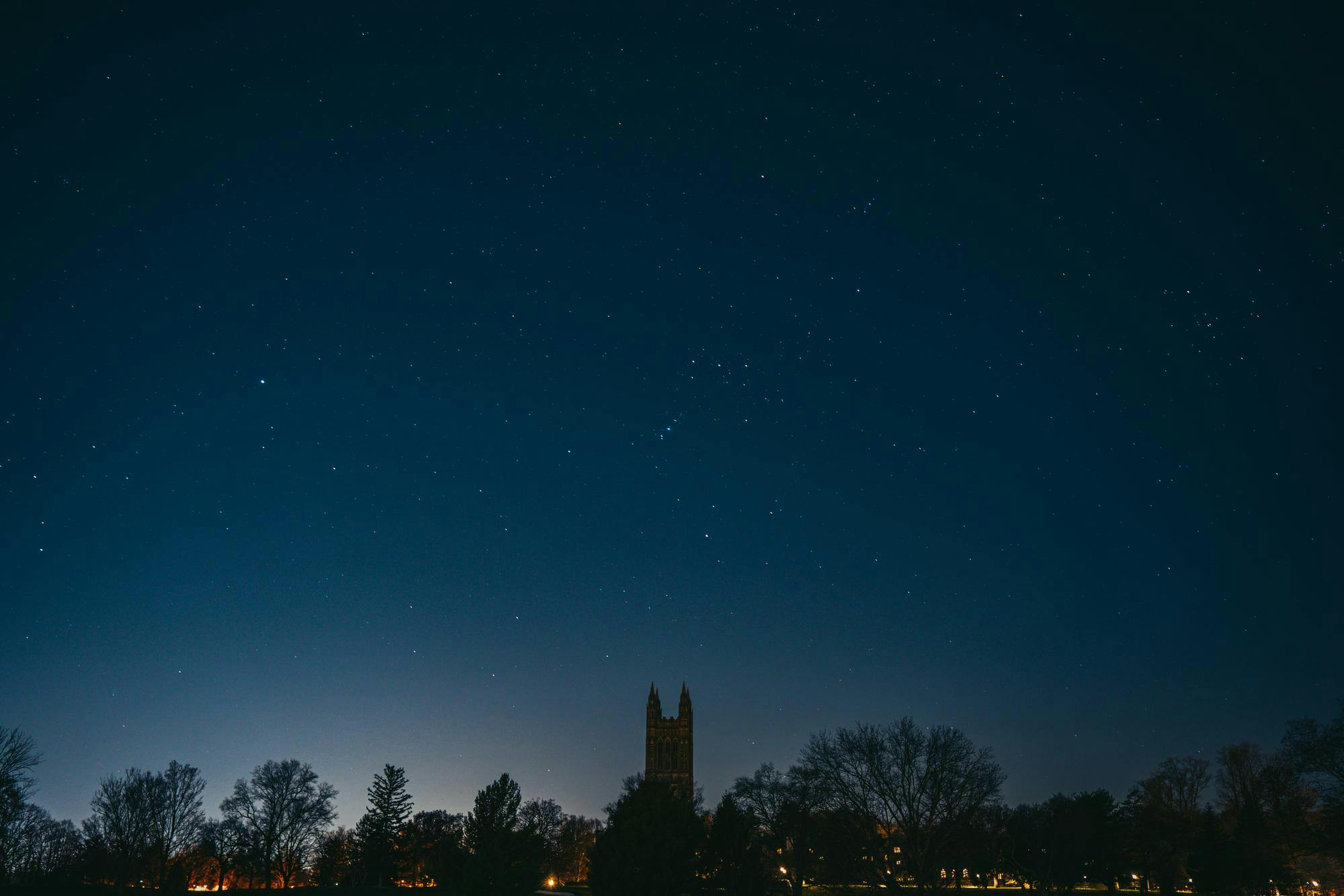 A dark night sky with a spattering of stars and the silhouette of a tall Gothic tower with four spires.