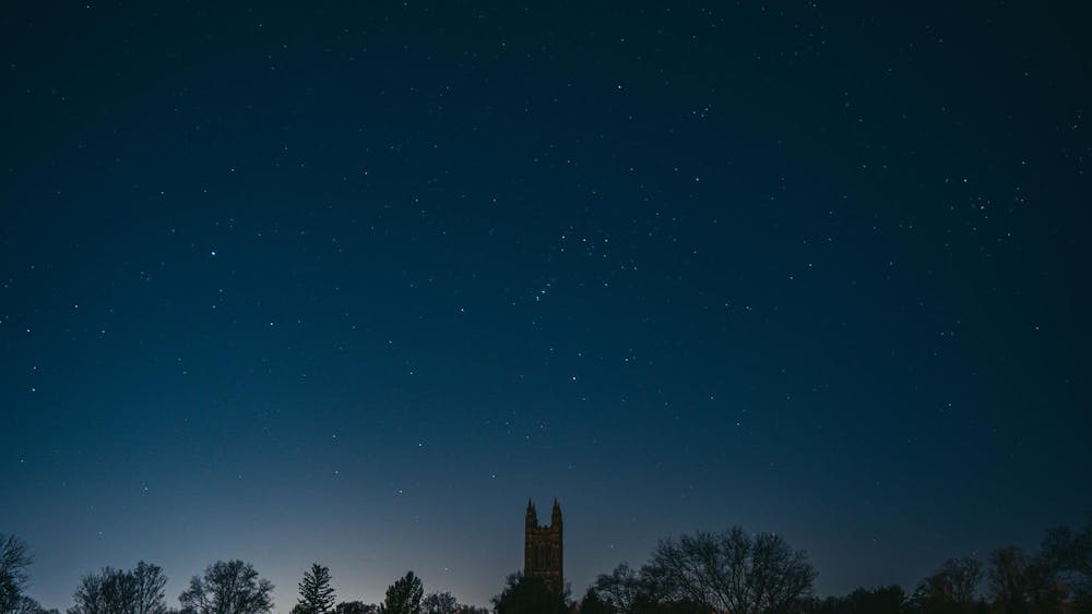 A dark night sky with a spattering of stars and the silhouette of a tall Gothic tower with four spires.