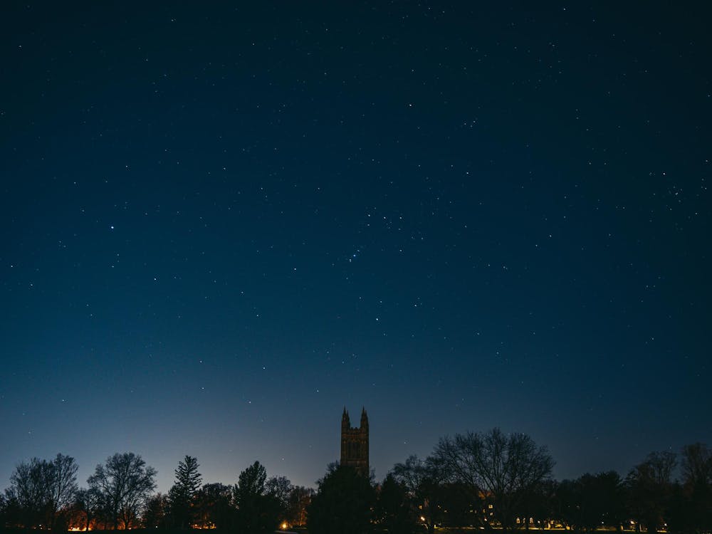 A dark night sky with a spattering of stars and the silhouette of a tall Gothic tower with four spires.