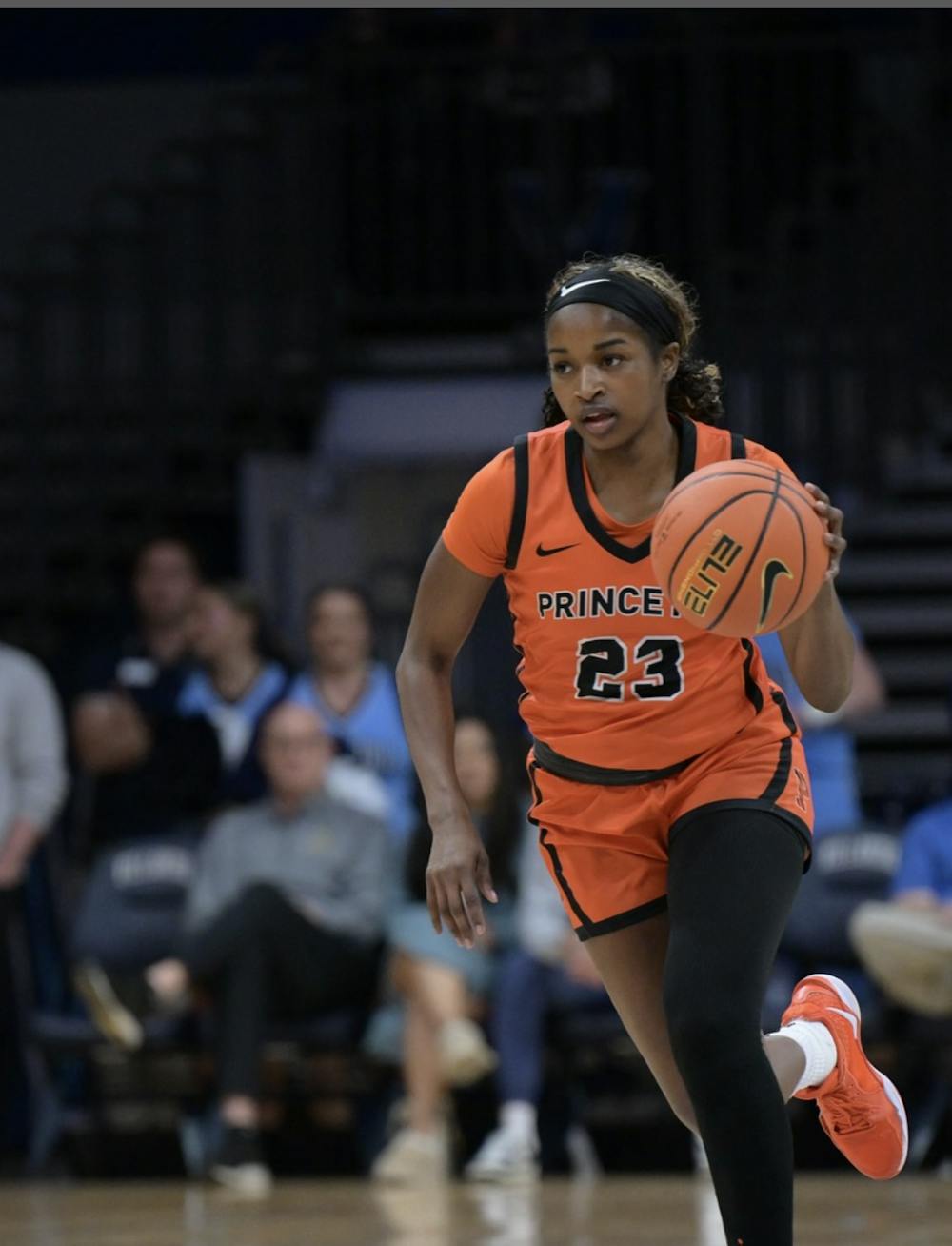A Princeton woman in an orange and black jersey dribbling a basketball. 
