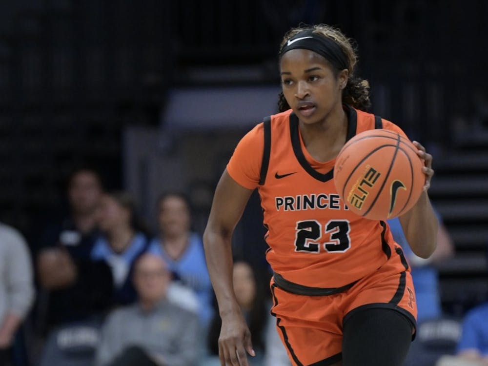 A Princeton woman in an orange and black jersey dribbling a basketball.