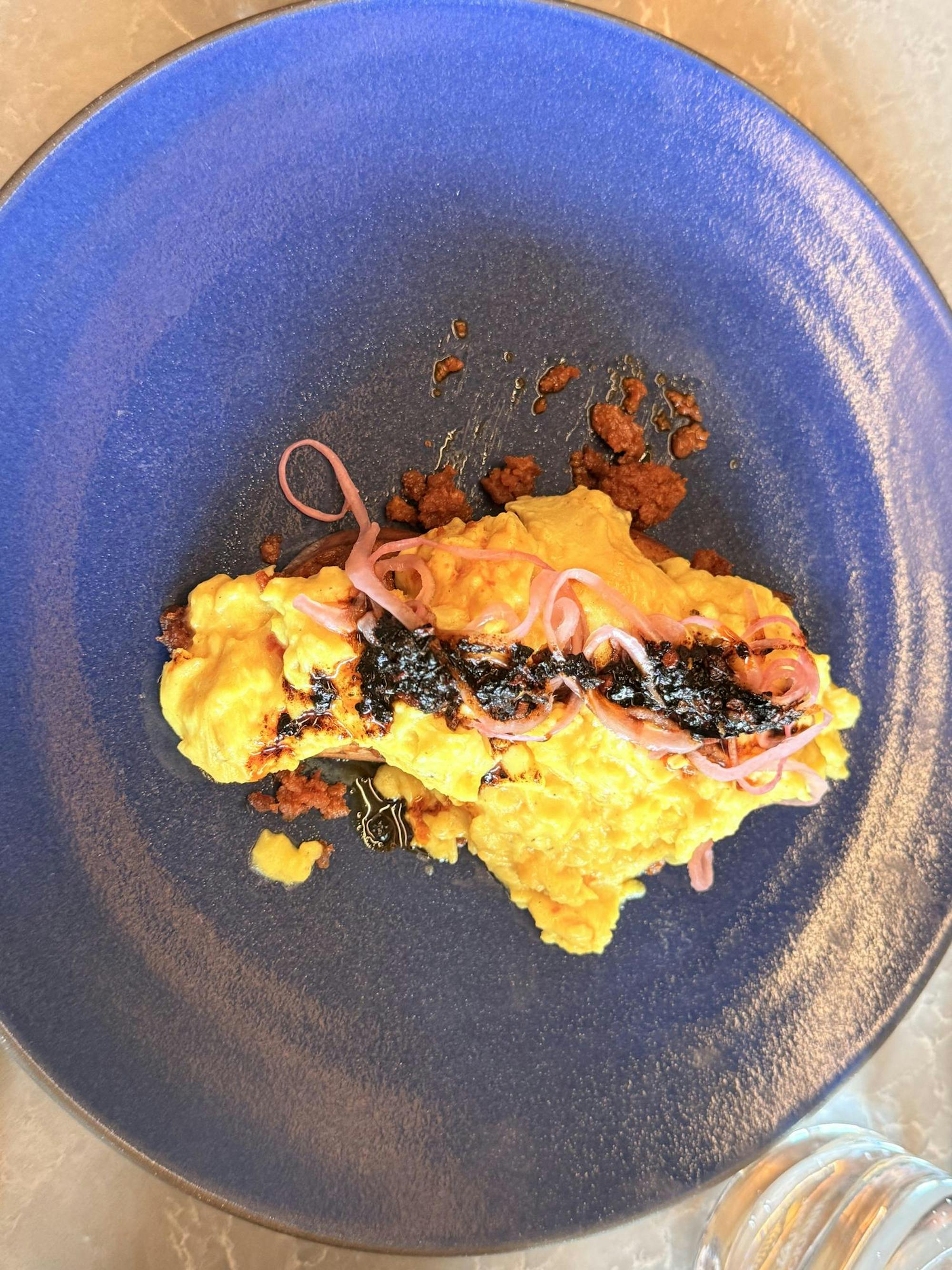 Scrambled eggs topped with pickled onions and salsa macha served on a blue plate.