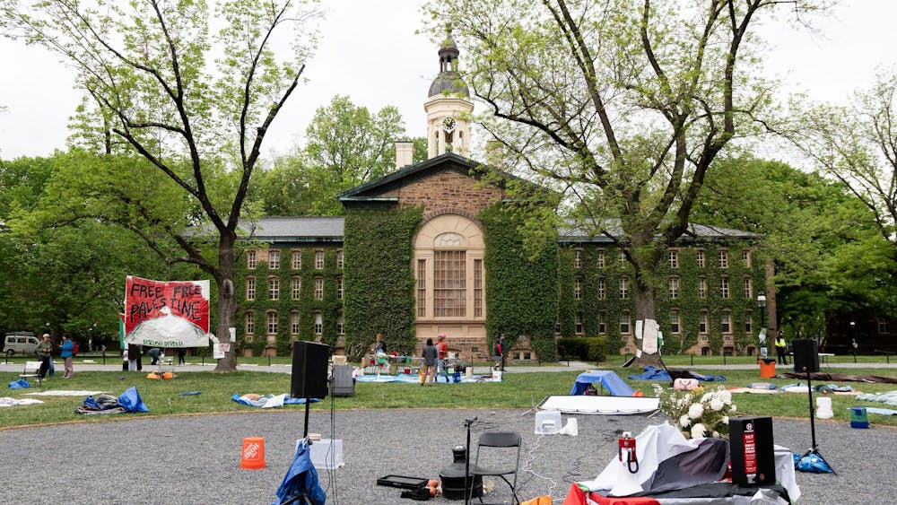 A large brick building covered in ivy overlooks a courtyard. Tarps are placed on the ground, and in the center there are speakers and a microphone, along with a folding chair.