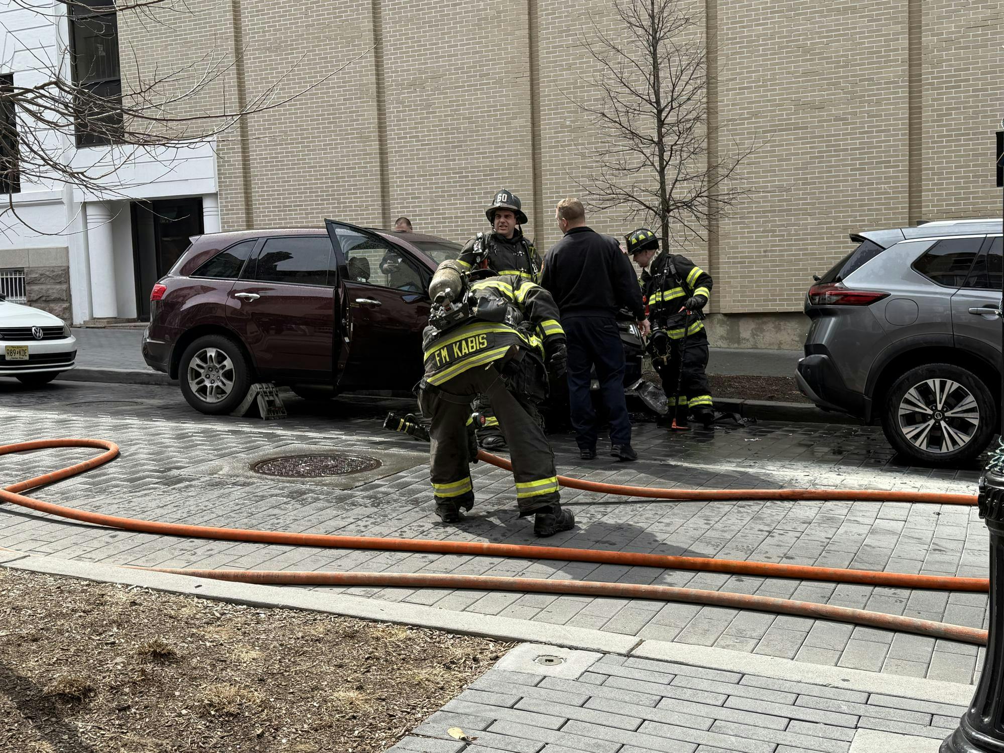 Firefighters stand beside a red Acura parked on Witherspoon Street. 