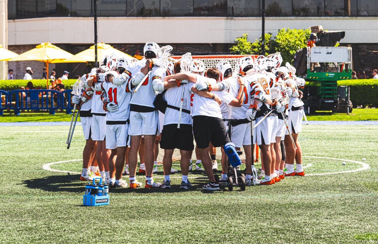 A group of men huddled together wearing white shorts and white jerseys on a grass field. 